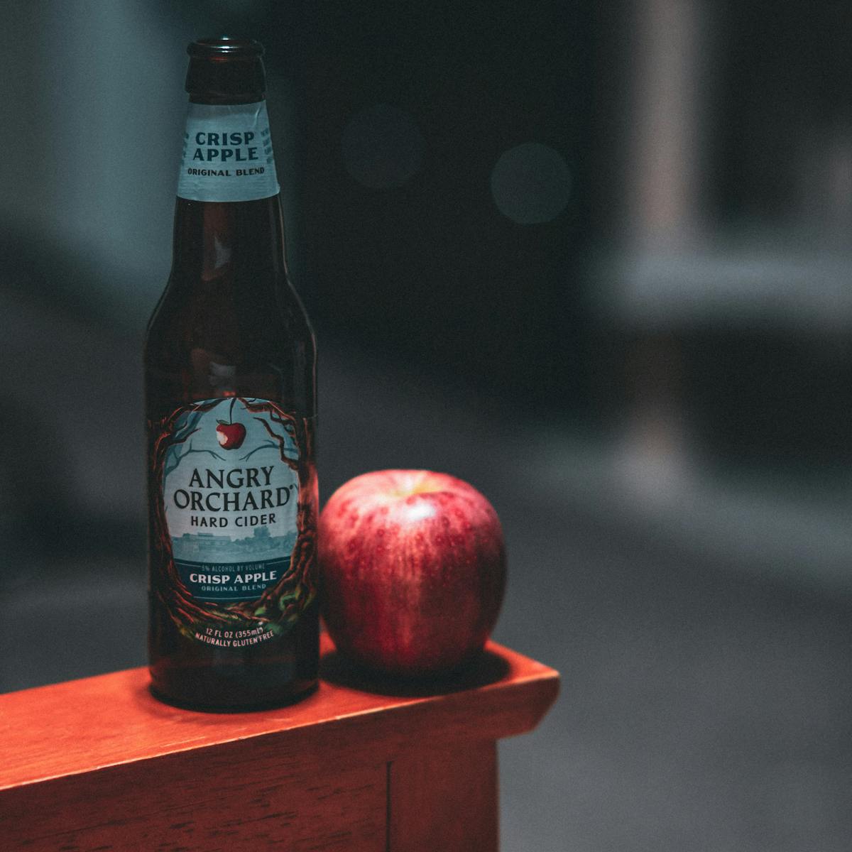 Bottle of apple cider vinegar next to a fresh red apple on a wooden table