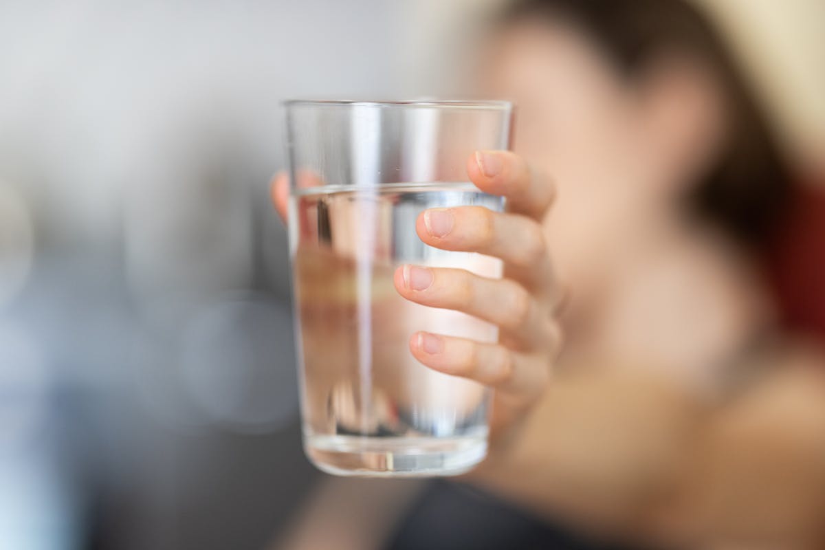 A hand holding a clear glass of water, ready to mix with apple cider vinegar